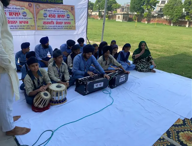 Pupils performing music outdoors with harmonium and tabla